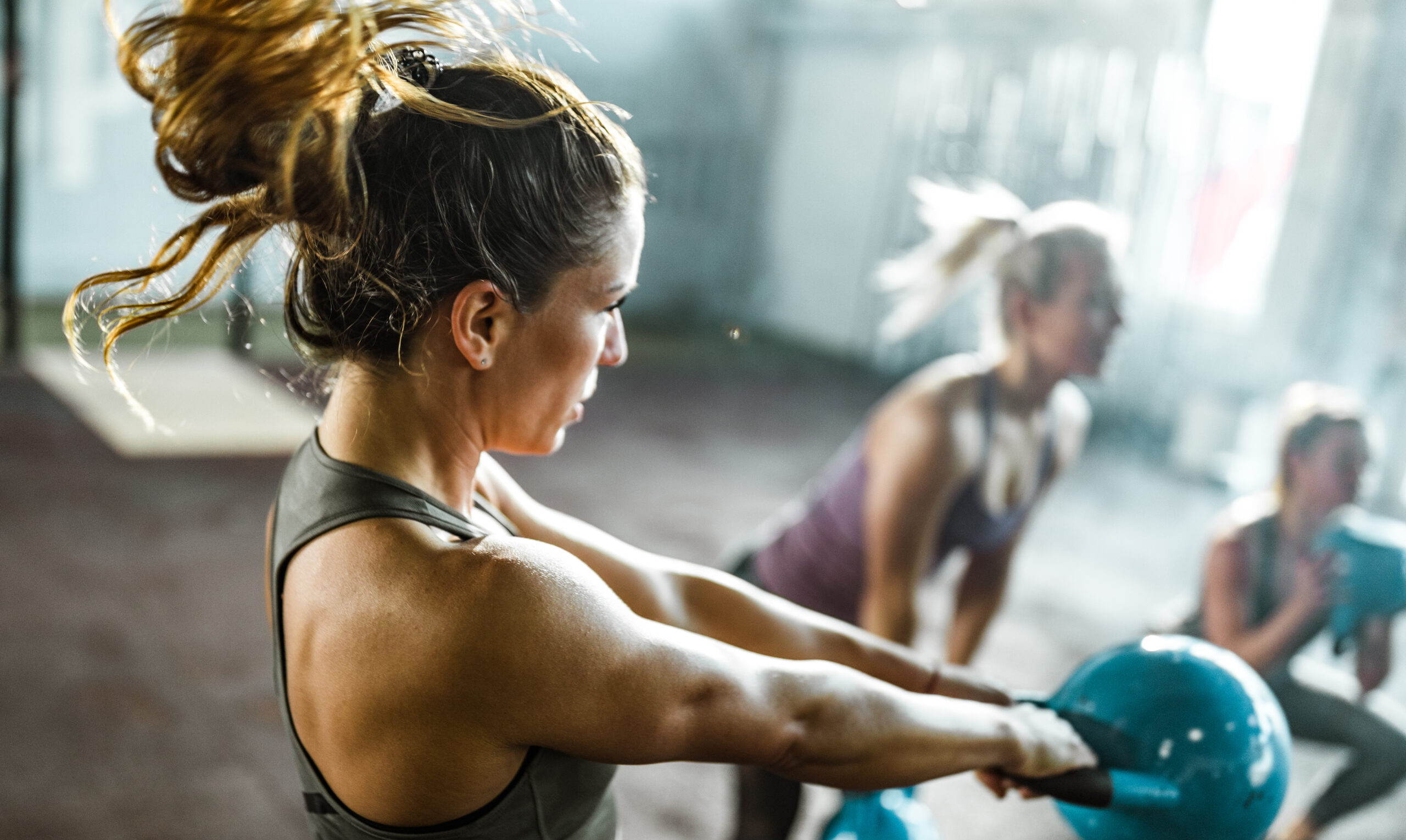 Determined athletic woman having gym training with kettle bell in a gym. Her friends are in the background.