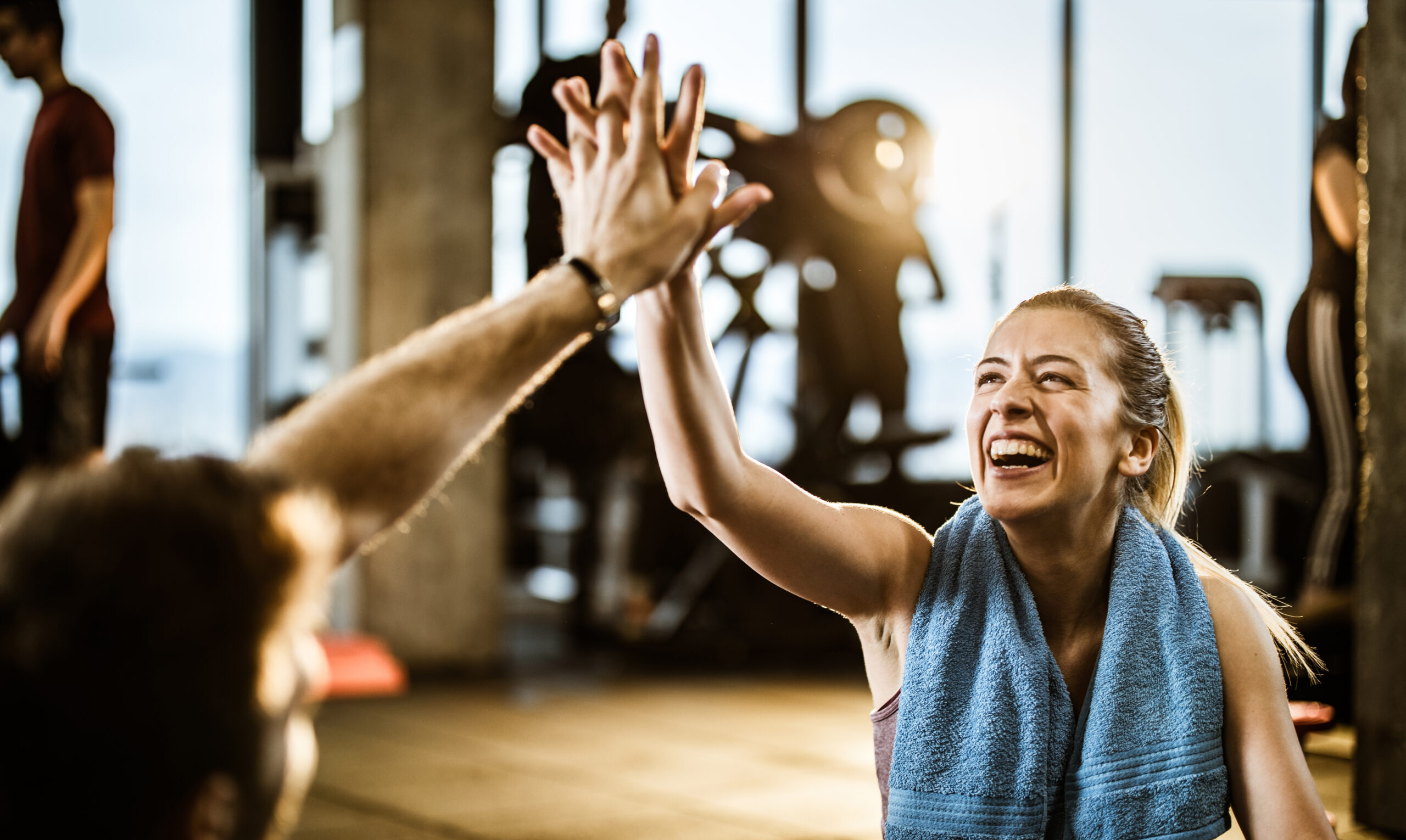 Happy female athlete having fun while giving her boyfriend high-five on a break in a gym.